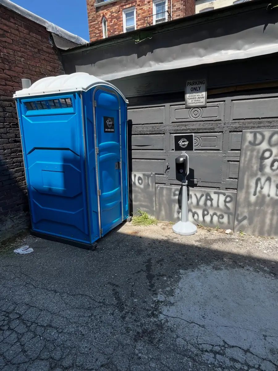 Blue porta potty in a paved alley behind a business