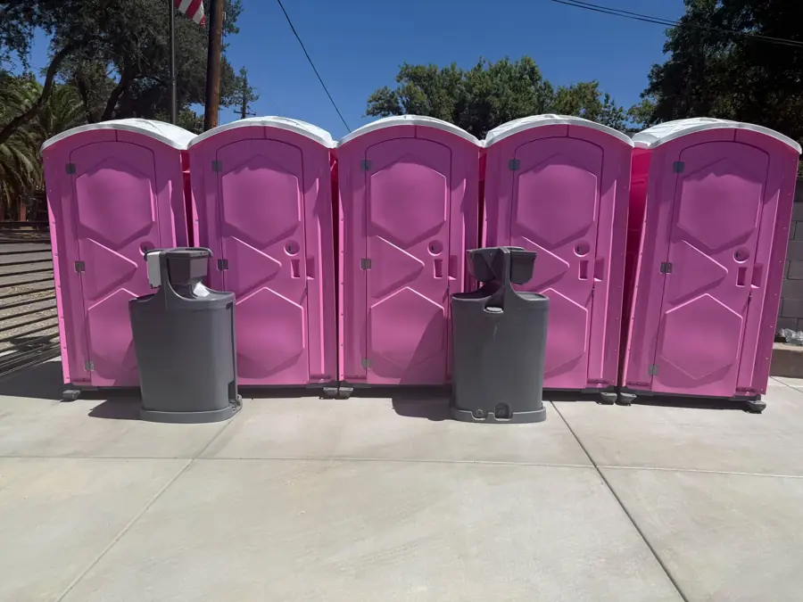 Five pink porta potties in a row with two gray hand wash stations