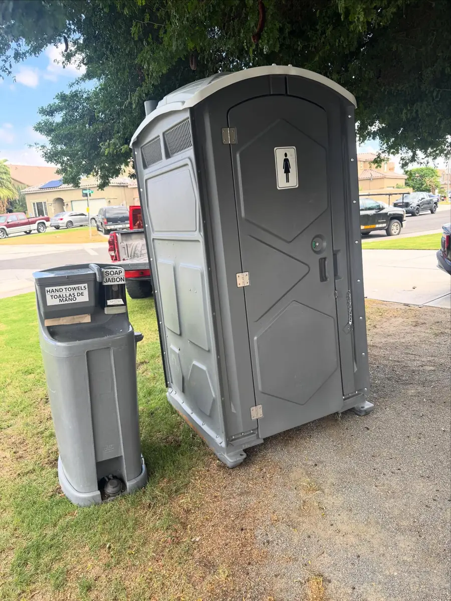 Gray porta potty next to a hand wash station on a lawn