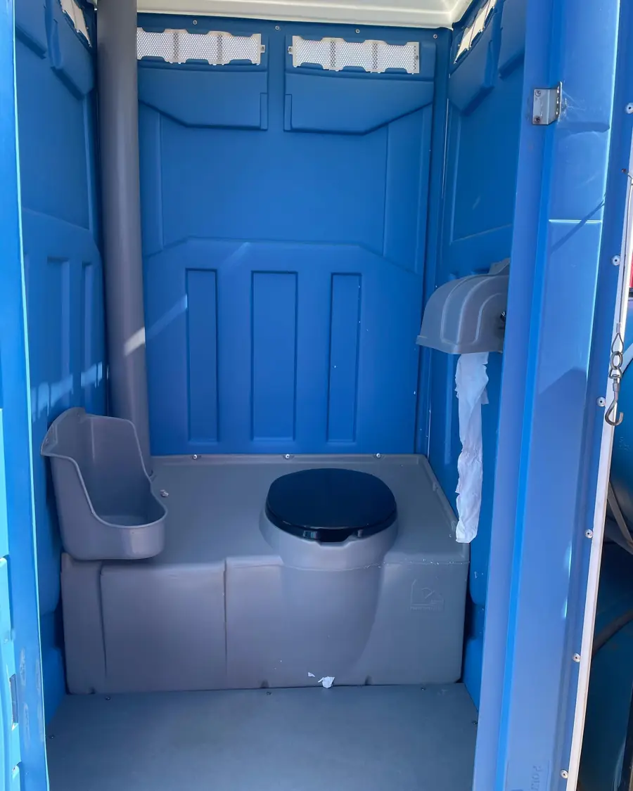 Inside a blue standard porta potty showing seat, urinal and toilet paper